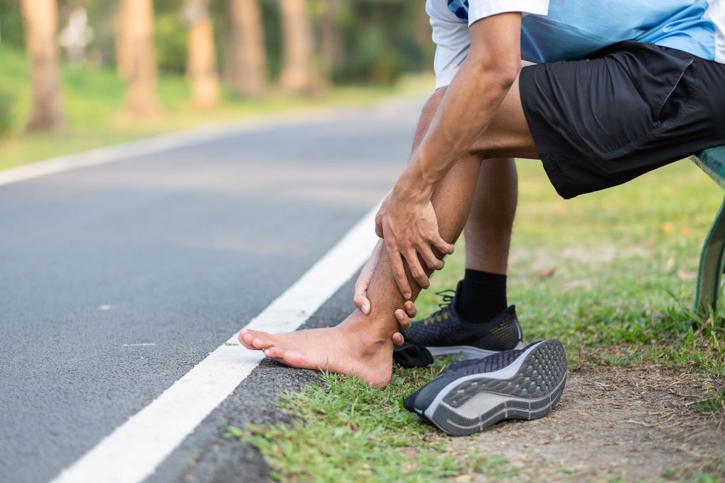 Man holding his foot and knee sprains near road.