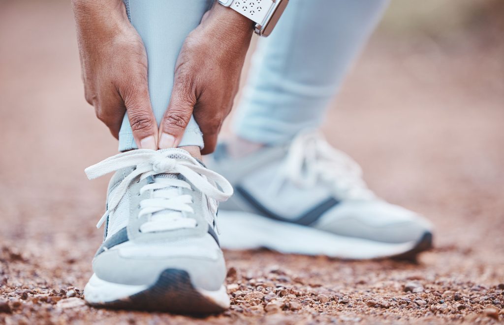 A person with blue pants and shoes holding their arthritis in feet.