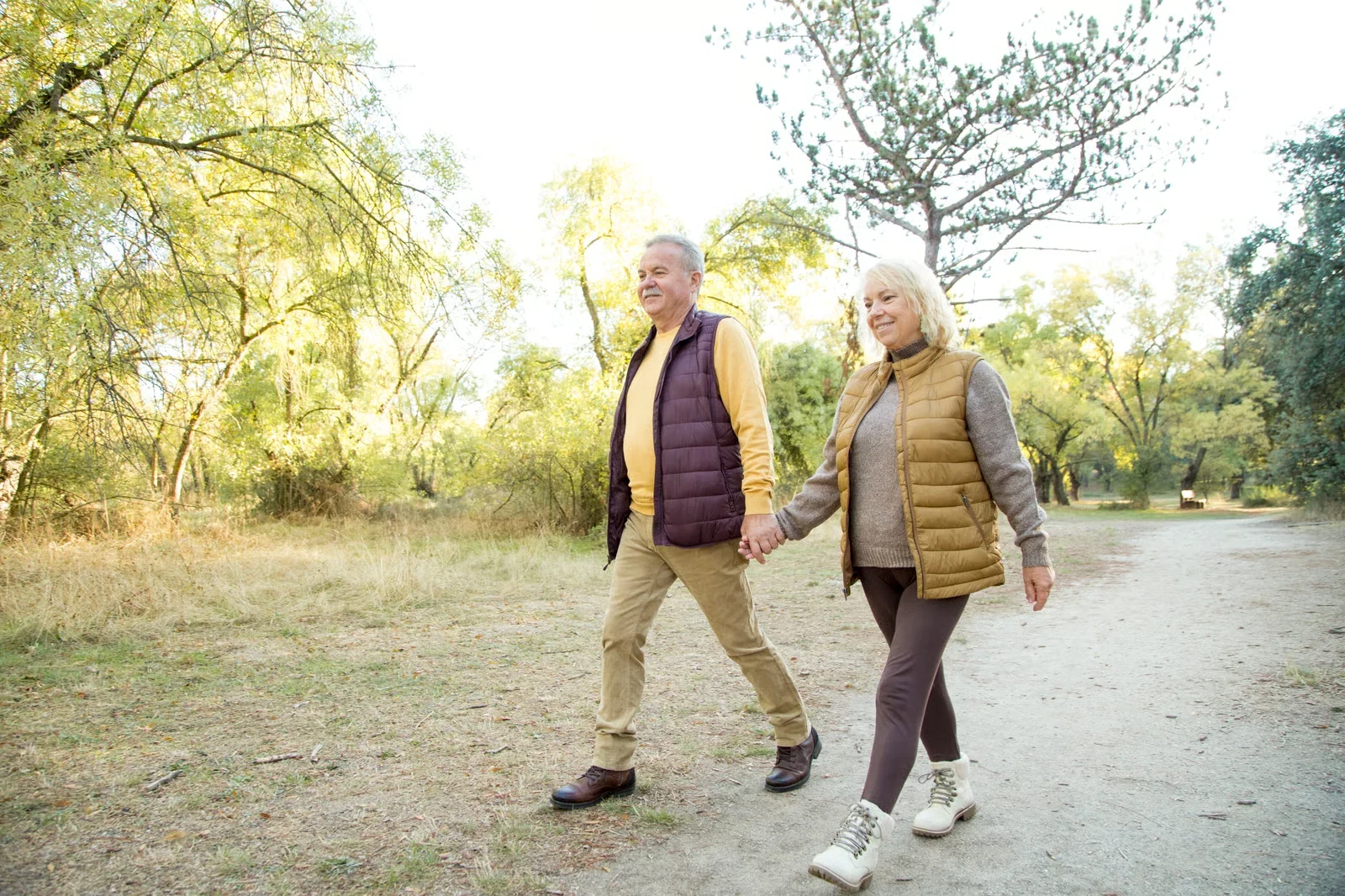 Older couple walking hand in hand along a park trail